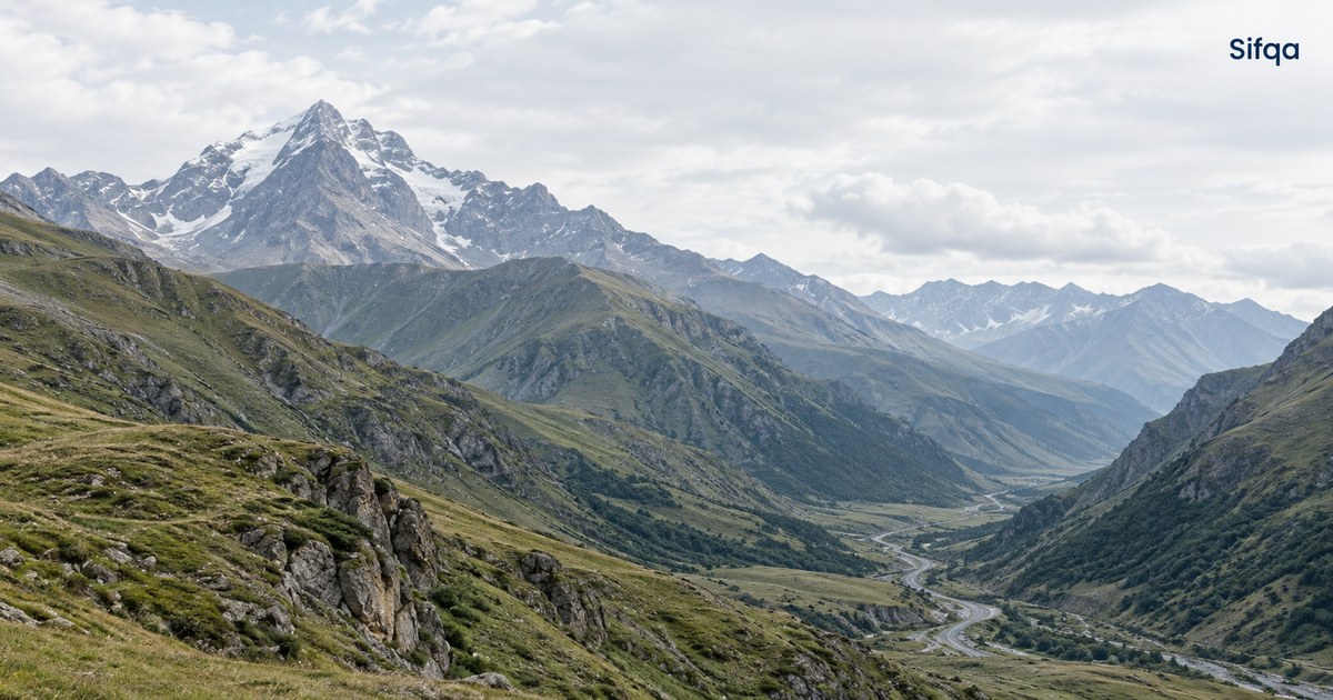 A snow-capped peak above a green valley in the Caucasus mountains, with a road winding along the floor.