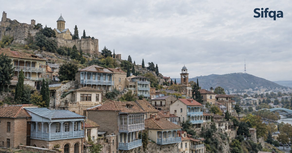 Old Tbilisi houses with carved wooden balconies on a hillside below a stone fortress.
