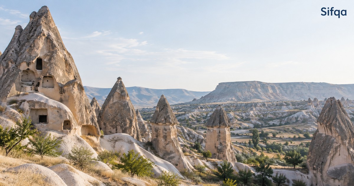 Cone-shaped rock formations with carved openings rising above a wide valley in Cappadocia.