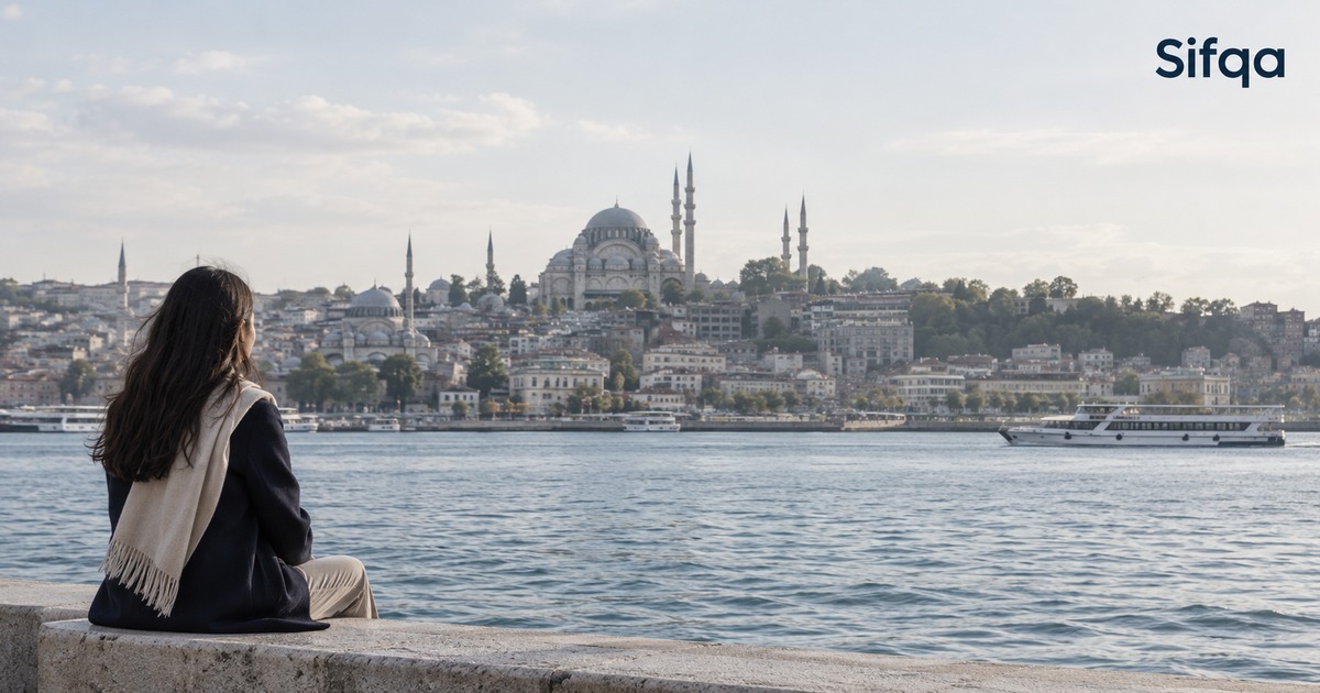 A person sitting on a waterfront wall looking across to the Istanbul skyline with its mosques and minarets.
