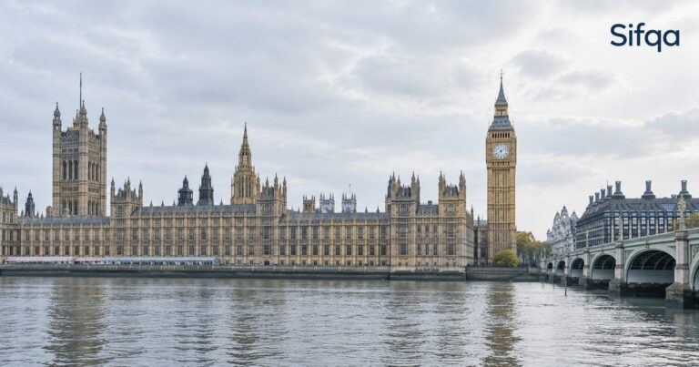The Houses of Parliament and Big Ben seen across the River Thames in London under a pale sky.