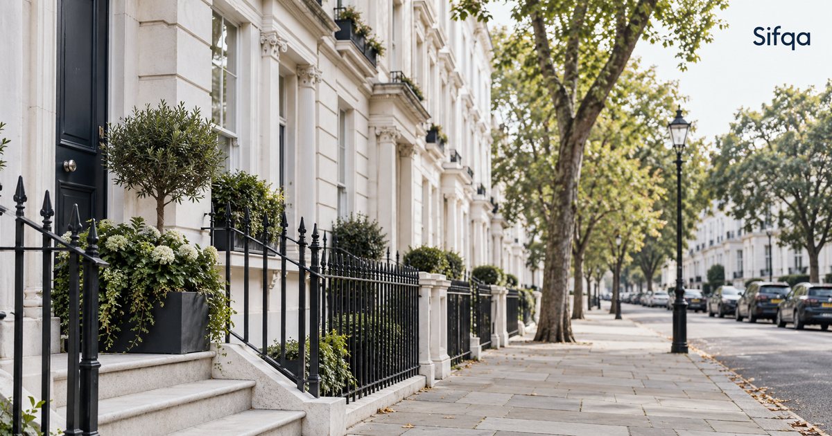 A row of white stucco London townhouses with black railings, beside a tree-lined pavement.